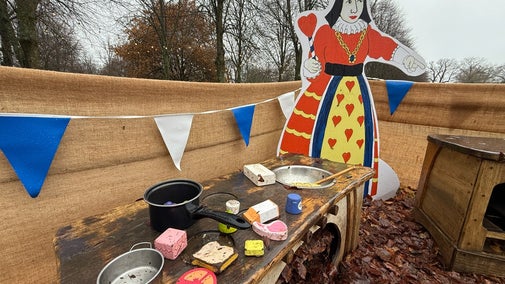 Alice's Christmas in Wonderland at Polesden Lacey 2025 - an outdoor play area for toddlers with a play kitchen, blue and white bunting and life-size picture of the Queen of Hearts